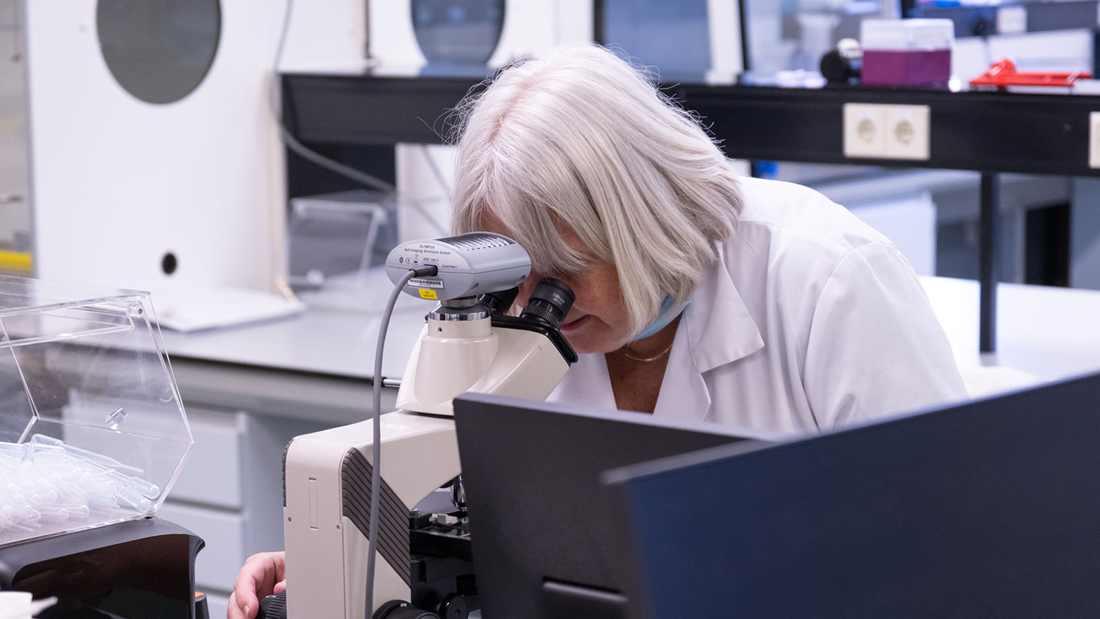 Female researcher with white hair looking into microscope
